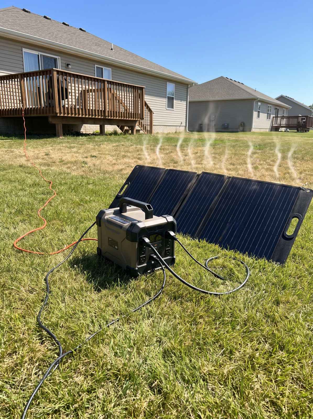 A portable power station charging from a folding solar panel on the grass in a sunny backyard