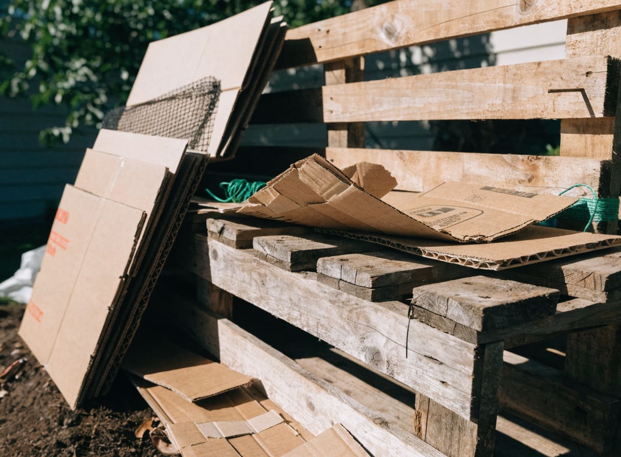 Wooden shipping pallets stacked beside broken-down cardboard boxes for composting