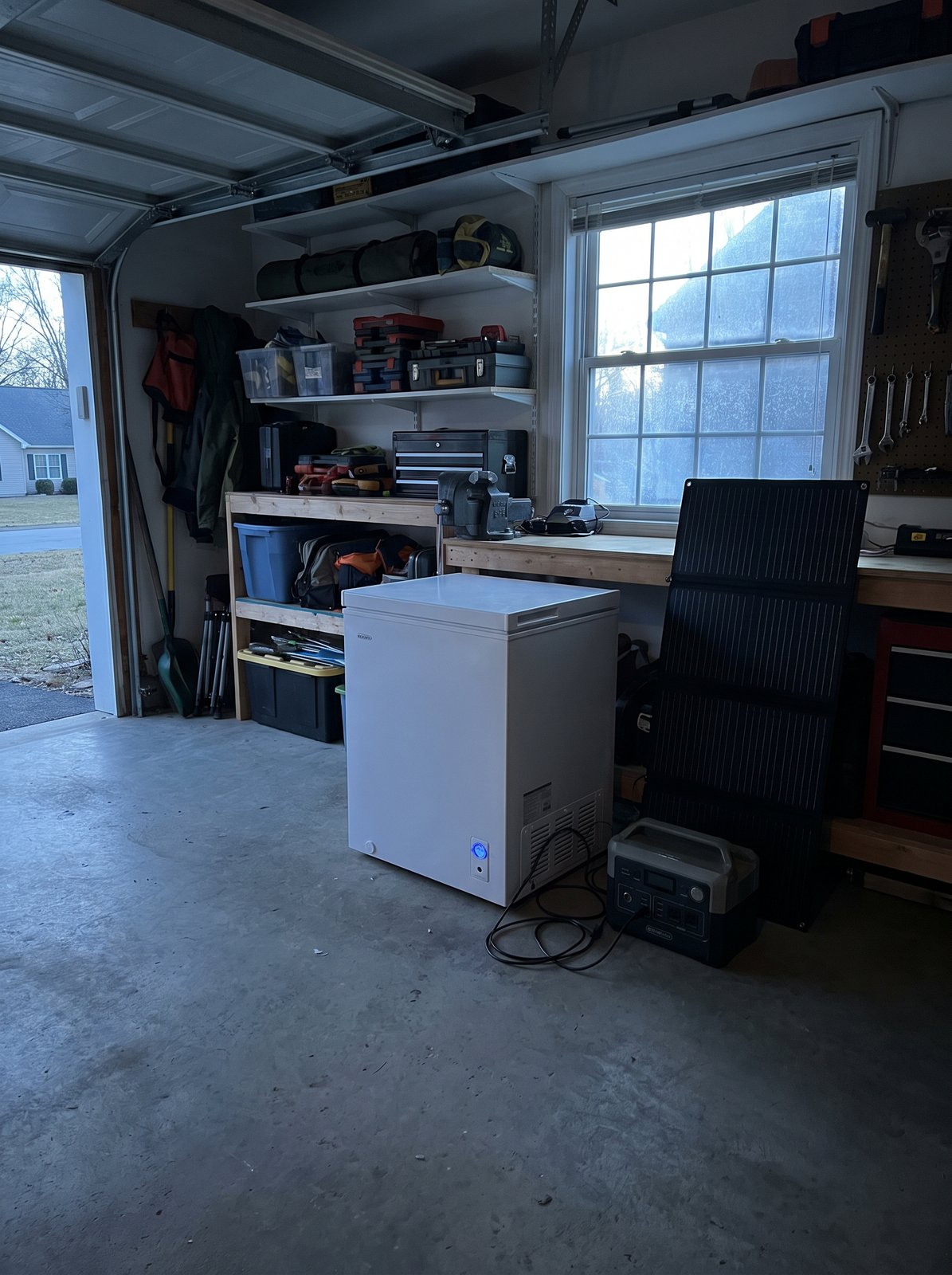 A chest freezer in a garage running off a portable power station and a small folding solar panel